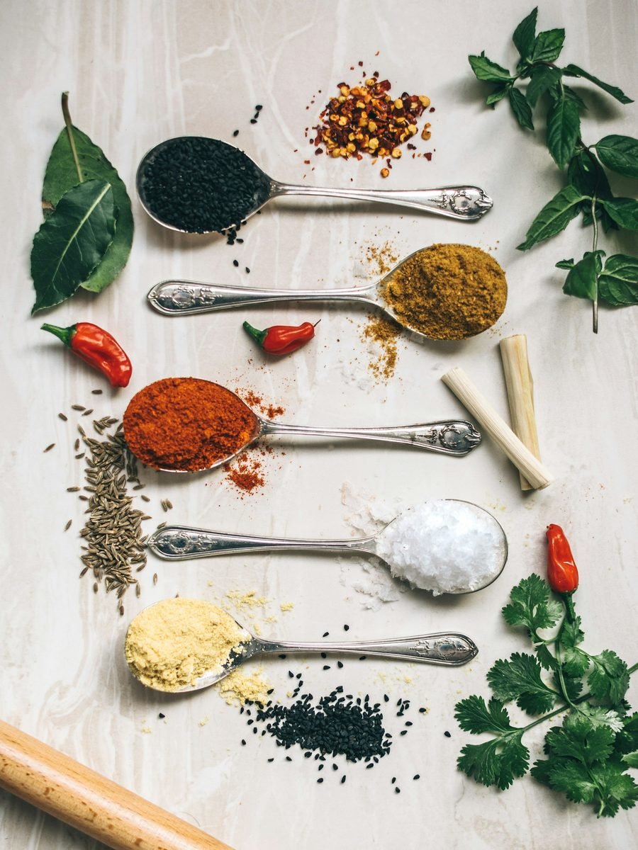 Assorted ground spices — chilli, turmeric, cumin — on silver spoons